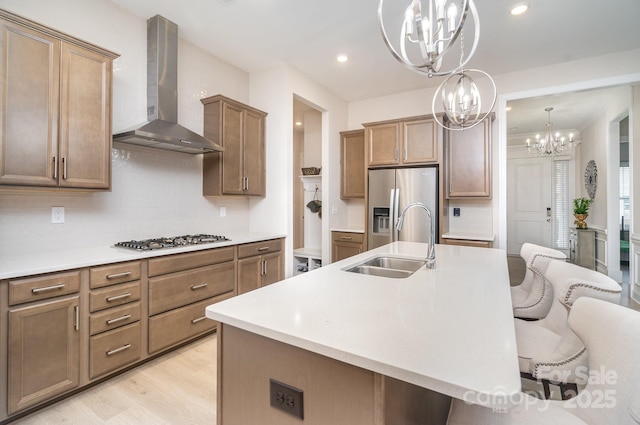 kitchen with an island with sink, wall chimney exhaust hood, a breakfast bar, and sink