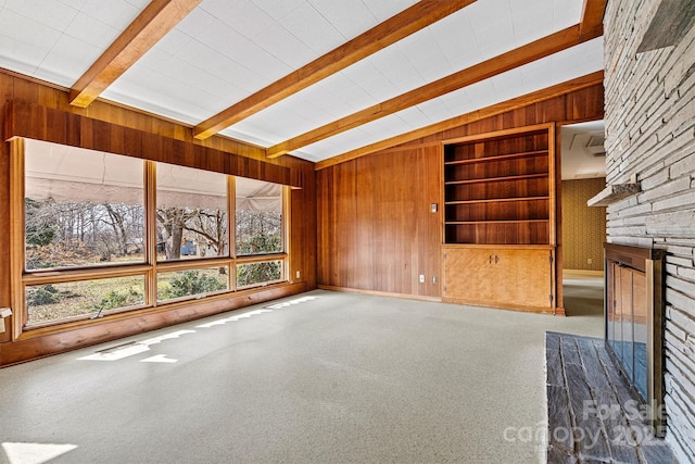 unfurnished living room featuring a fireplace, wooden walls, lofted ceiling with beams, carpet flooring, and built in shelves