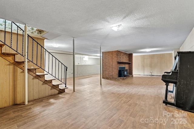 basement featuring light hardwood / wood-style floors, a textured ceiling, and a wood stove