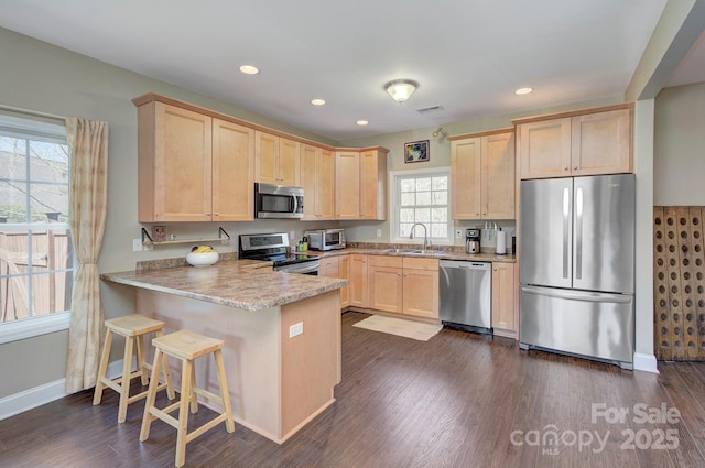 kitchen featuring appliances with stainless steel finishes, light brown cabinetry, sink, a breakfast bar area, and kitchen peninsula