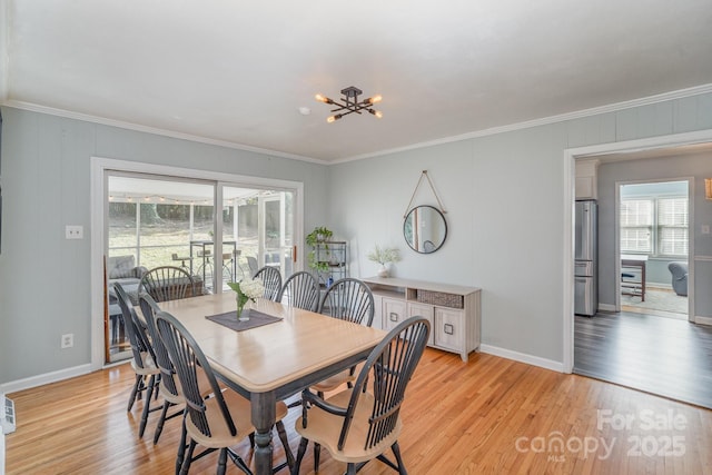 dining space with ornamental molding, an inviting chandelier, and light hardwood / wood-style floors