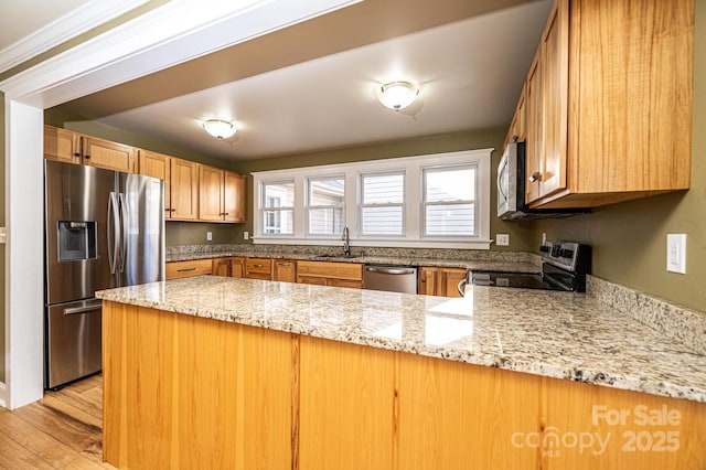 kitchen featuring sink, light stone counters, light wood-type flooring, appliances with stainless steel finishes, and kitchen peninsula