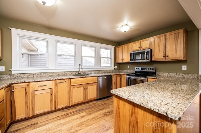 kitchen featuring sink, light hardwood / wood-style flooring, stainless steel appliances, light stone countertops, and kitchen peninsula