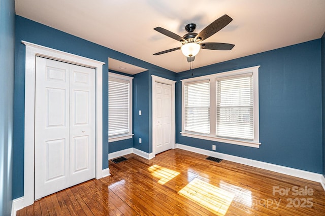 unfurnished bedroom with multiple closets, dark hardwood / wood-style floors, and ceiling fan