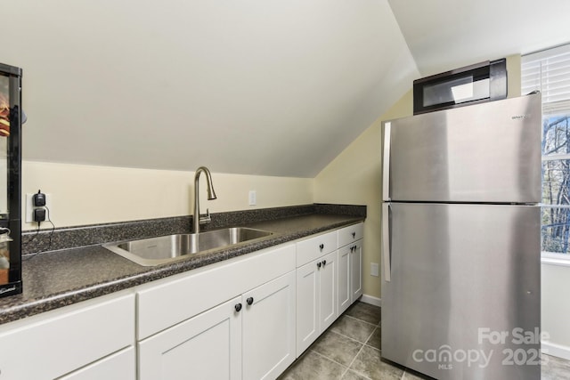 kitchen with lofted ceiling, sink, white cabinetry, light tile patterned floors, and stainless steel refrigerator