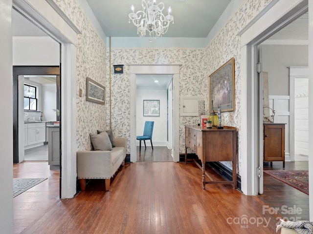 hallway with crown molding, a notable chandelier, hardwood / wood-style floors, and wallpapered walls