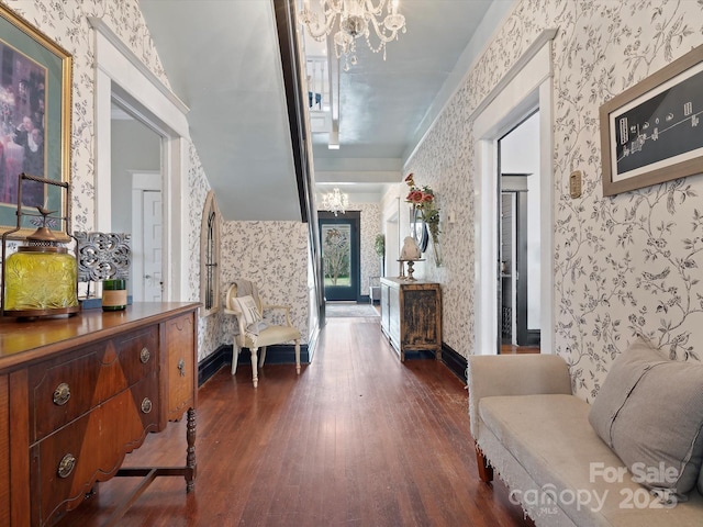 hall featuring dark wood-type flooring, a notable chandelier, baseboards, and wallpapered walls