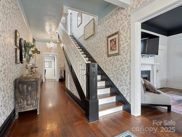 staircase featuring wallpapered walls, a fireplace, a chandelier, and hardwood / wood-style flooring