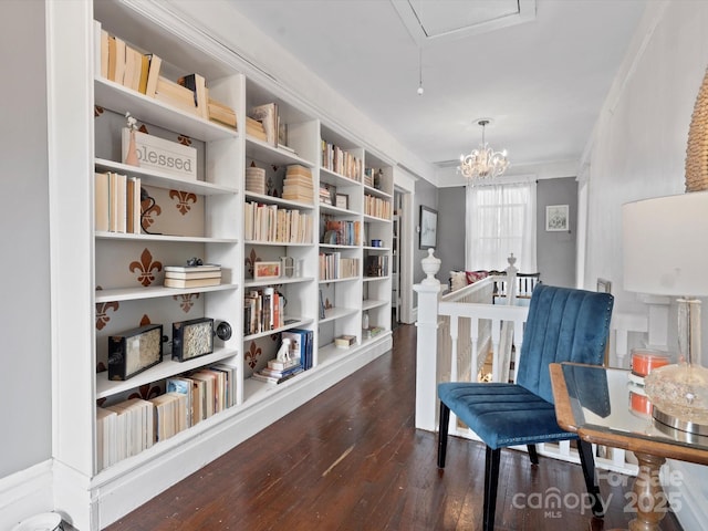 sitting room featuring dark wood-style flooring, a notable chandelier, crown molding, attic access, and an upstairs landing