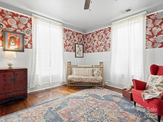 bedroom featuring wallpapered walls, wood-type flooring, visible vents, and a wainscoted wall