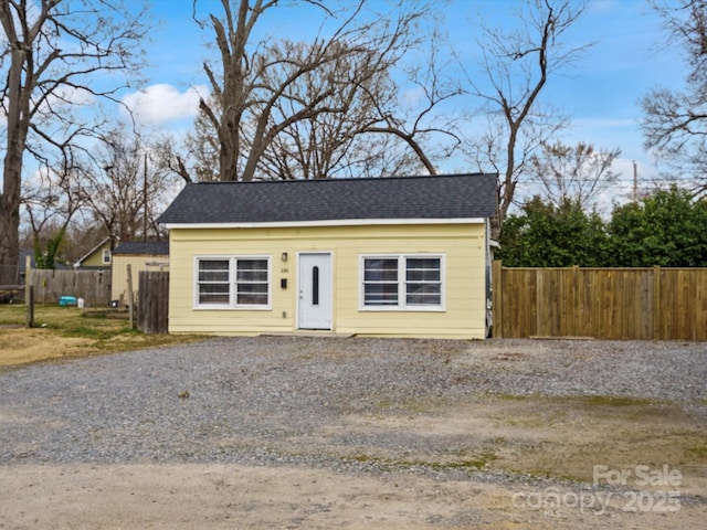 view of front of property with gravel driveway, a shingled roof, and fence