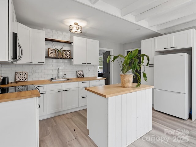 kitchen with a sink, wood counters, freestanding refrigerator, open shelves, and stainless steel microwave