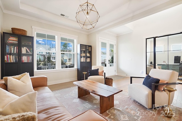 living room with crown molding, a chandelier, light wood-type flooring, and a tray ceiling