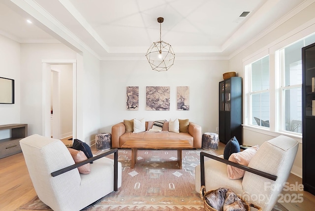 living room with a notable chandelier, a tray ceiling, ornamental molding, and light hardwood / wood-style floors