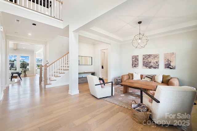 living room with crown molding, an inviting chandelier, and light wood-type flooring