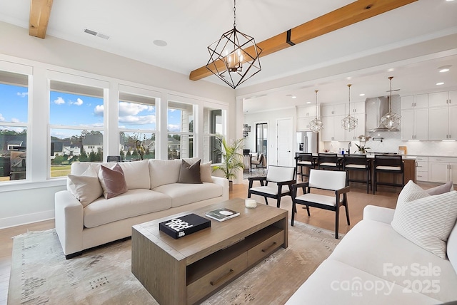 living room with beamed ceiling, a chandelier, and light hardwood / wood-style flooring