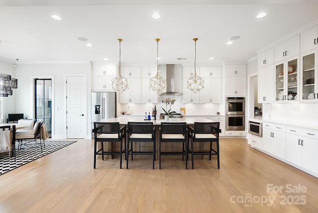 kitchen featuring appliances with stainless steel finishes, decorative light fixtures, an island with sink, a kitchen breakfast bar, and wall chimney range hood