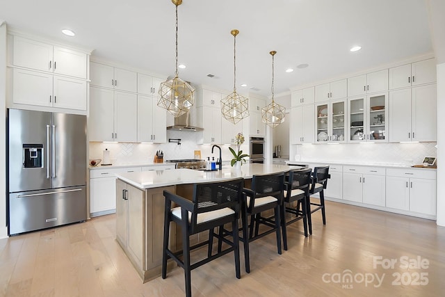 kitchen featuring a breakfast bar area, stainless steel appliances, white cabinets, a center island with sink, and decorative light fixtures