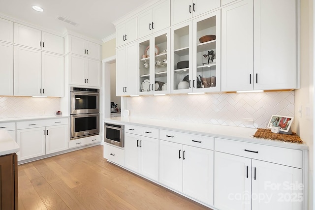 kitchen featuring white cabinetry, double oven, tasteful backsplash, and light wood-type flooring