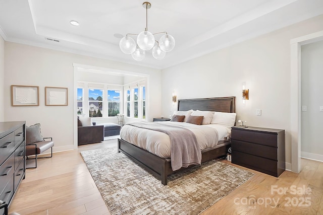 bedroom with an inviting chandelier, a raised ceiling, and light hardwood / wood-style floors