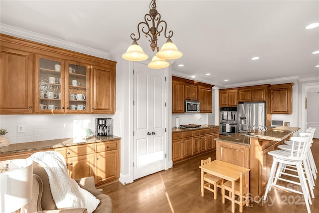 kitchen with pendant lighting, appliances with stainless steel finishes, hardwood / wood-style floors, light stone counters, and ornamental molding