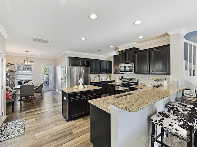 kitchen with a breakfast bar, sink, decorative light fixtures, appliances with stainless steel finishes, and kitchen peninsula