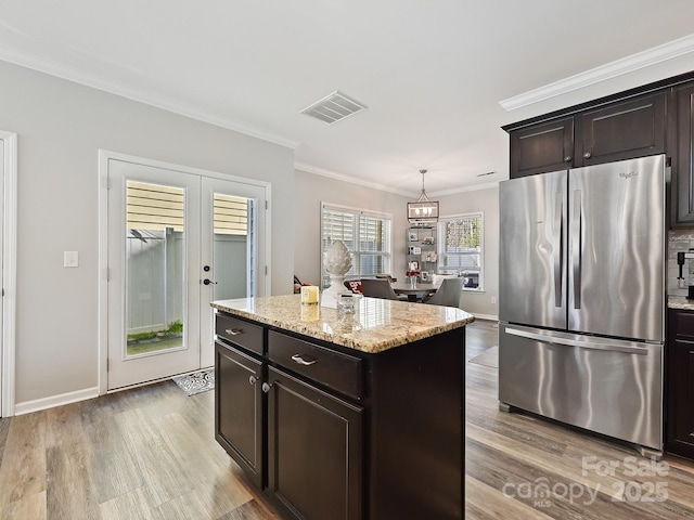 kitchen featuring crown molding, a center island, hanging light fixtures, stainless steel fridge, and light stone countertops