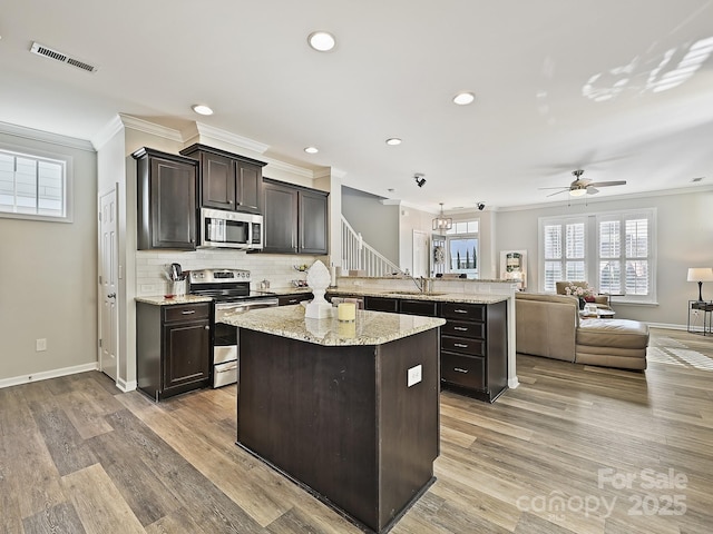 kitchen with a kitchen island, hanging light fixtures, ornamental molding, stainless steel appliances, and dark brown cabinets