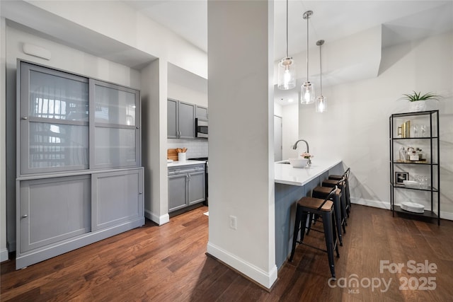 kitchen with dark wood-type flooring, a breakfast bar, sink, gray cabinetry, and decorative light fixtures