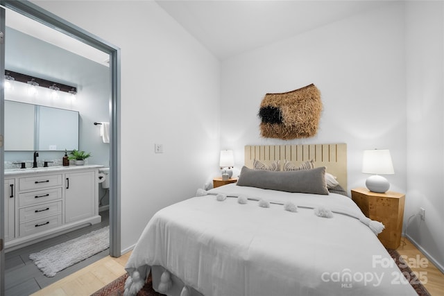 bedroom with vaulted ceiling, sink, and light hardwood / wood-style flooring