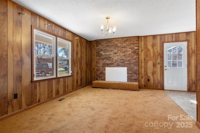 interior space featuring wood walls, a healthy amount of sunlight, a textured ceiling, and a notable chandelier