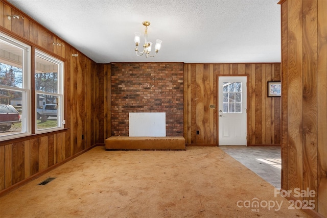 unfurnished living room featuring carpet flooring, wooden walls, a chandelier, and a textured ceiling