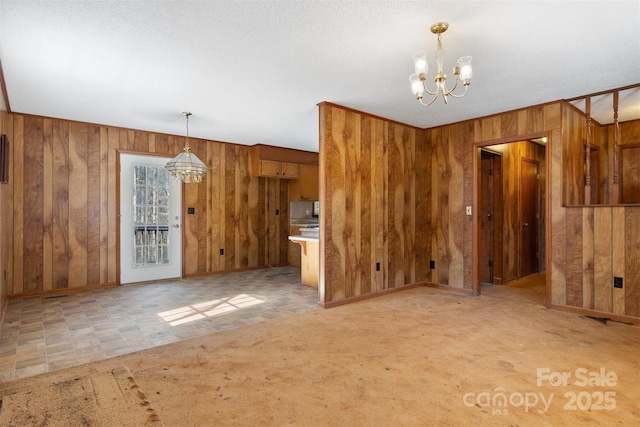 unfurnished living room featuring wooden walls, light carpet, and an inviting chandelier