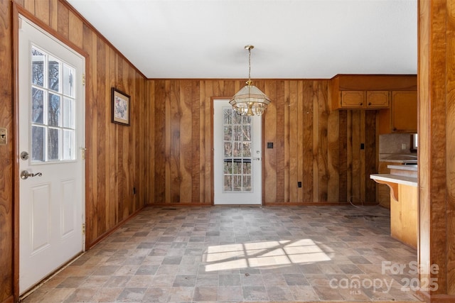 unfurnished dining area featuring a chandelier and wooden walls