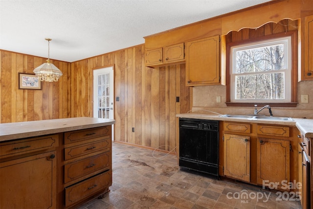 kitchen with sink, wood walls, a textured ceiling, dishwasher, and pendant lighting