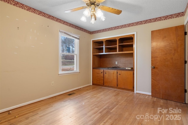 interior space with a textured ceiling, ceiling fan, and light wood-type flooring