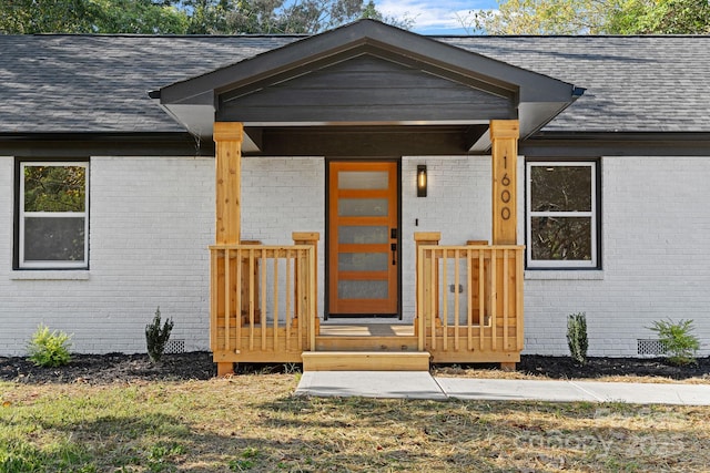 property entrance with a shingled roof, crawl space, brick siding, and a porch