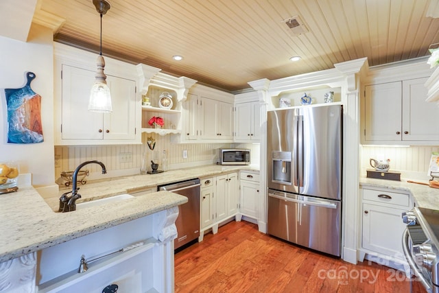 kitchen with light stone counters, appliances with stainless steel finishes, hanging light fixtures, and white cabinets