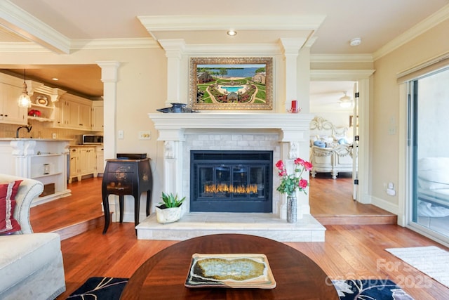 living room featuring hardwood / wood-style flooring, ornamental molding, a brick fireplace, and ornate columns