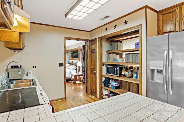 kitchen featuring visible vents, light wood-style flooring, appliances with stainless steel finishes, brown cabinets, and ornamental molding