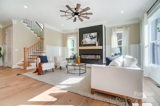 living area featuring ornamental molding, ceiling fan, a fireplace, and light hardwood / wood-style floors