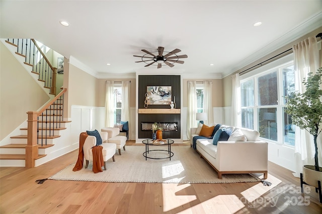 living room with crown molding, a fireplace, light hardwood / wood-style floors, and ceiling fan