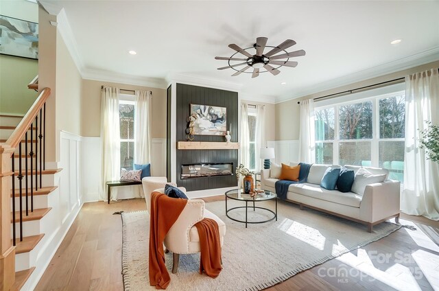 living room with light hardwood / wood-style flooring, ornamental molding, a large fireplace, and ceiling fan