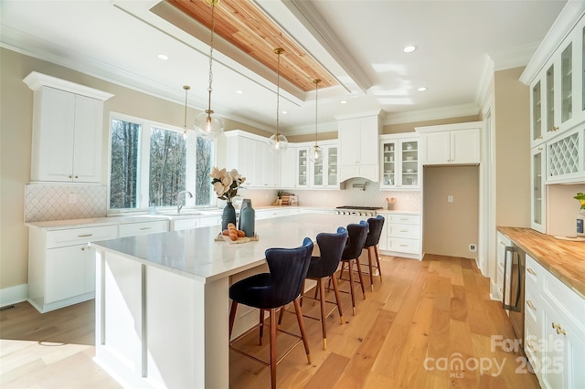 kitchen featuring pendant lighting, crown molding, a center island, white cabinets, and light wood-type flooring