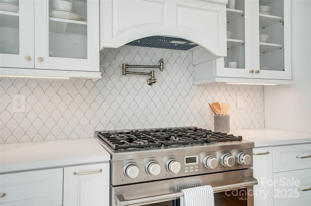 kitchen featuring backsplash, stainless steel gas range, white cabinets, and custom exhaust hood