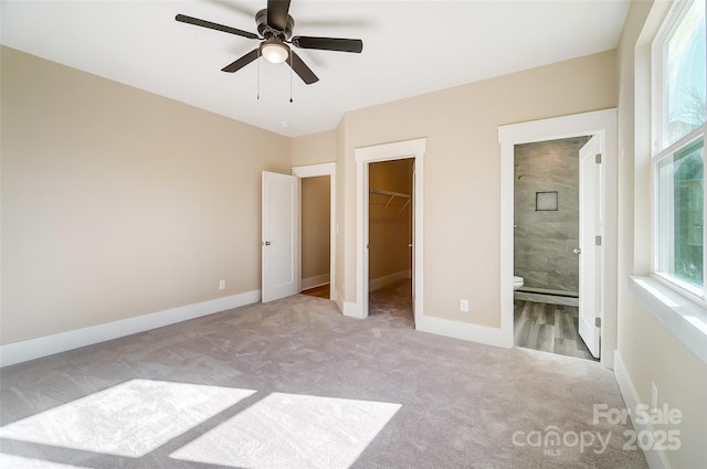 unfurnished bedroom with ceiling fan, ensuite bathroom, a spacious closet, light colored carpet, and a closet