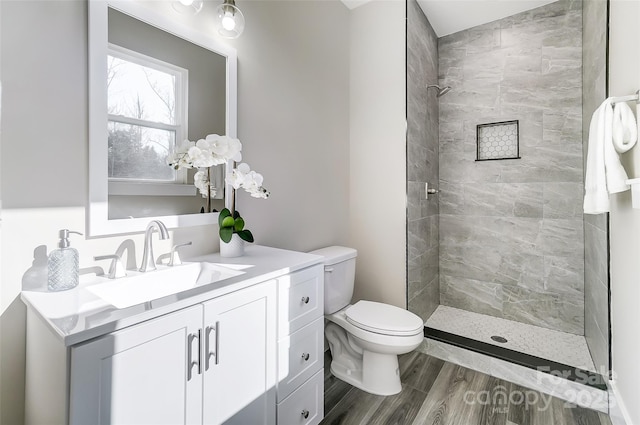 bathroom featuring hardwood / wood-style flooring, vanity, tiled shower, and toilet