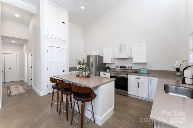 kitchen with sink, a center island, white cabinetry, stainless steel appliances, and wall chimney exhaust hood