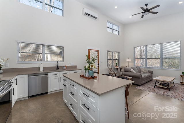 kitchen with a wall mounted air conditioner, concrete flooring, appliances with stainless steel finishes, and white cabinetry