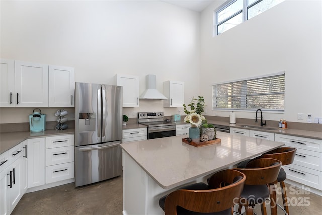 kitchen featuring a kitchen island, sink, appliances with stainless steel finishes, wall chimney range hood, and a kitchen breakfast bar